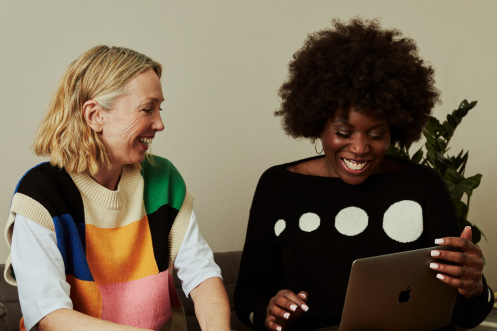 Two women smiling & laughing looking at a laptop
